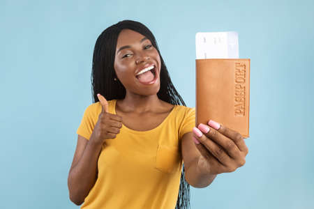 African American Female Showing Travel Tickets Gesturing Thumbs-Up, Blue Backgroundの写真素材