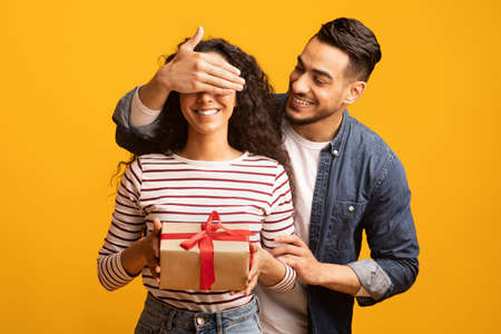 Surprise Gift. Romantic arab man covering his girlfriends eyes and giving presentの写真素材