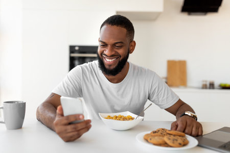 Black man texting on his smartphone having breakfast at homeの写真素材