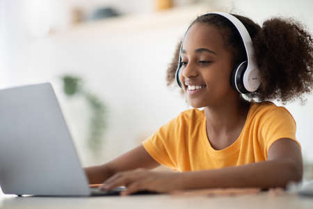 Cheerful black girl studying online, using laptop and headset