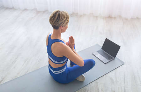 Woman meditating sitting in lotus position on mat with pcの写真素材