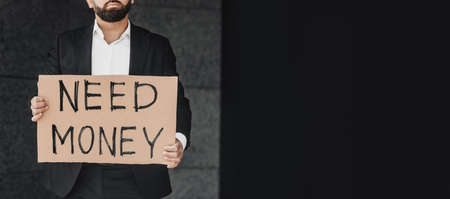 Unrecognizable businessman in suit holding sign with words NEED MONEY while standing outdoors, panorama with free spaceの写真素材