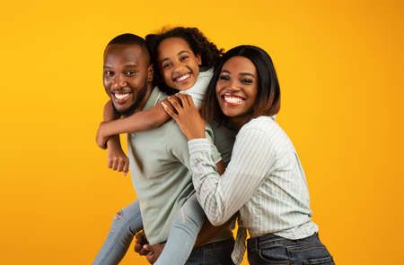 Time with family. Overjoyed african american family laughing and posing to camera isolated over yellow studio wallの写真素材