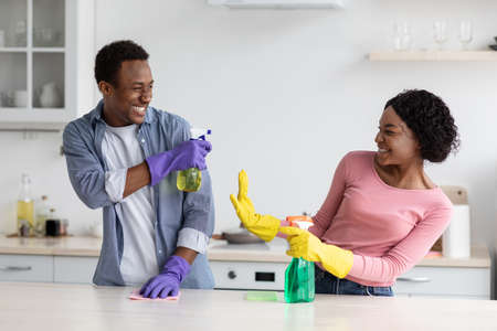 Cheerful black house-keepers having fun while cleaning kitchenの写真素材