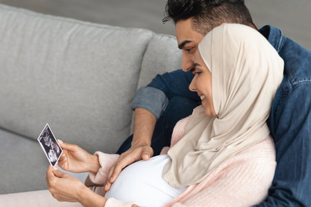 Happy Pregnant Arabic Woman And Her Husband Looking At Baby Sonogram Pictureの写真素材
