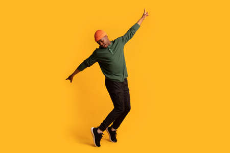 Cheerful young african american man standing on tiptoes over yellow background
