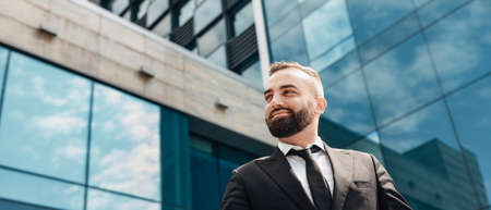Portrait of wealthy mature man in suit looking at copy space, happy businessman posing over glass office buildingの写真素材