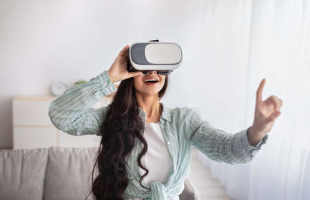 Happy Indian woman in VR glasses interacting with virtual reality, exploring cyberspace, playing...