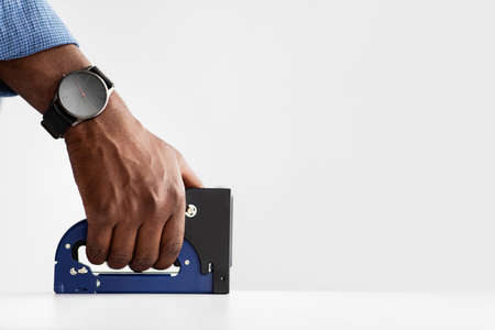 Unrecognizable african american carpenter using staple gun tool making furniture, working with white...