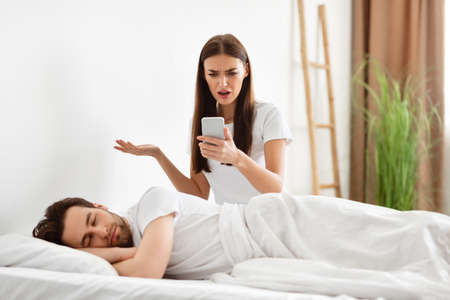 Shocked Woman Reading Cheating Husbands Messages On Cellphone In Bedroom