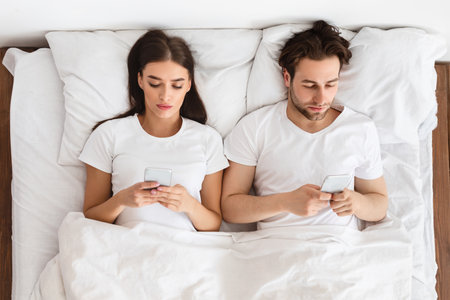 Couple Using Mobile Phones Lying In Bed At Home, Top-Viewの写真素材