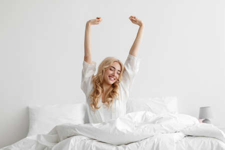 Good morning, smiling young lady waking up fully rested on white bedding, relax at home at weekend, vacationの写真素材