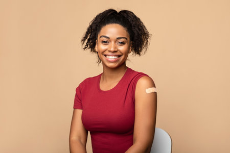 Happy black lady with adhesive bandage on shoulder after  vaccine shot looking at camera on beige backgroundの写真素材