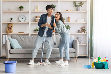 Funny asian couple singing songs while cleaning apartment, copy spaceの写真素材