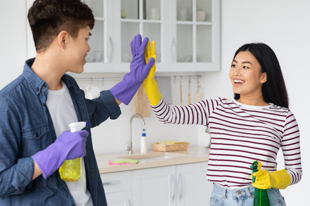 Happy asian couple house-keepers giving each other high fiveの写真素材