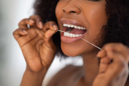 Unrecognizable Afro woman cleaning teeth with dental floss at home, closeup. Oral hygiene, wellness,...