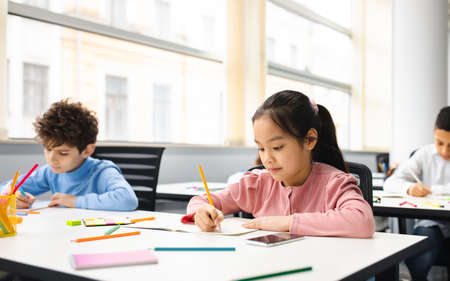 Portrait of asian girl sitting in classroom and writingの写真素材