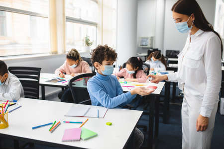 Teacher applying antibacterial sanitizer on pupils handsの写真素材