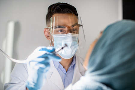 Arab Dentist Doctor In Medical Mask And Face Shield Checking Patients Teethの写真素材