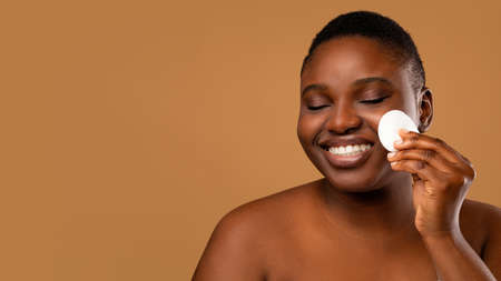 Portrait of chubby black woman cleaning skin by cotton pad