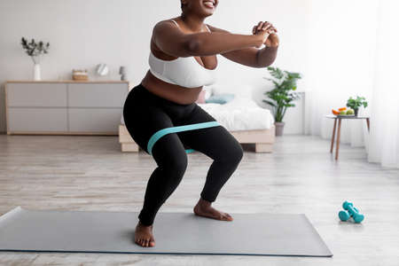 Cropped view of curvy woman squatting with rubber band on domestic workout