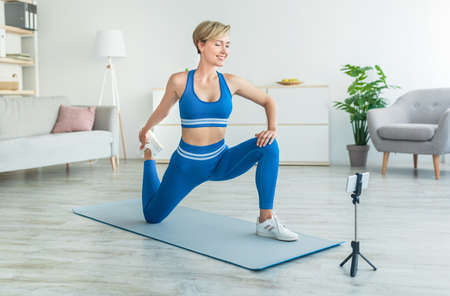 Cheerful woman stretching leg in front of smartphone