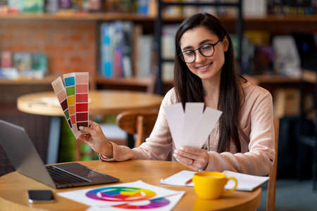 Creative latin woman web-designer working with color palette while sitting at cafe with laptop, free spaceの写真素材
