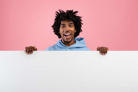 Positive black teenager with white blank poster on pink studio background, mockup for your ad designの写真素材