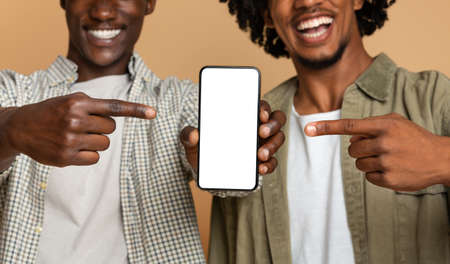 Two Cheerful Black Guys Pointing At Smartphone With Blank White Screenの写真素材