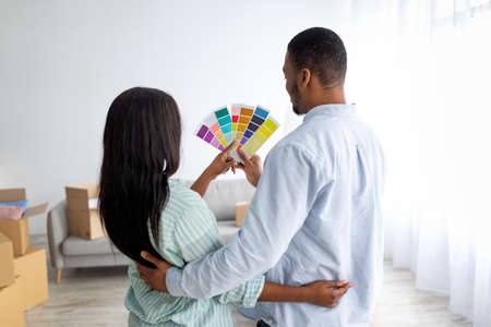 Renovation planning. Young black couple choosing color for walls painting, holding palette, back viewの写真素材