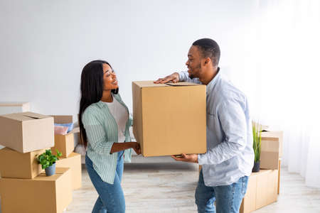 Happy young black couple carrying cardboard box together, helping each other on moving day, free...