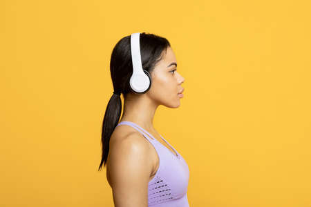 Music and sports concept. Profile portrait of african american sportswoman in wireless headphones, yellow backgroundの写真素材