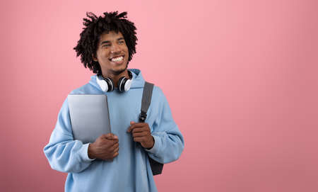 Positive African American teen student with backpack, tablet pc and headphones studying online on pink backgroundの写真素材