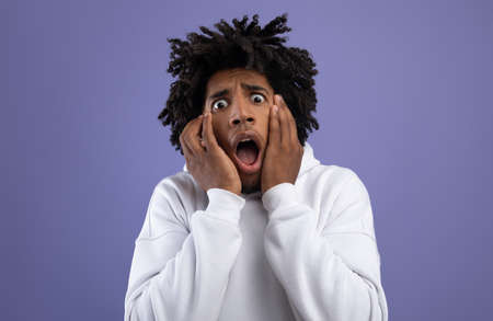 Black teen guy feeling scared, shouting in panic on violet studio background