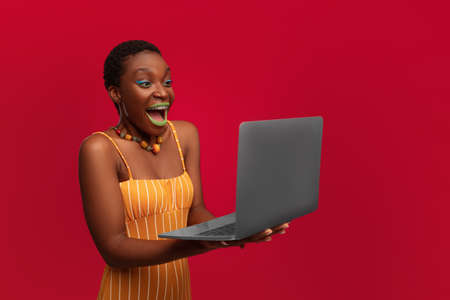 Amazed young black woman holding modern laptop