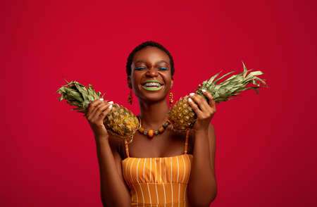 Ecstatic afro american woman holding pinapples and laughingの写真素材