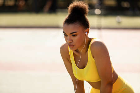 Sporty black woman in yellow sportswear resting listening to musicの写真素材