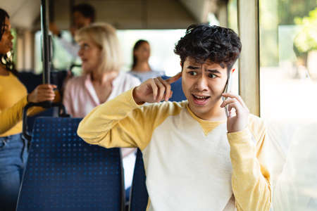Confused asian guy talking on phone holding finger in earの写真素材