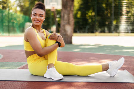 Smiling Black Sporty Woman In Yellow Sportswear Stretching Leg Outdoors