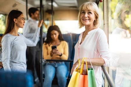 Beautiful smiling mature woman taking bus, holding shopping bagsの写真素材