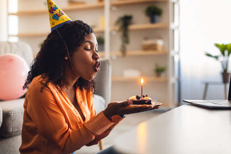 Female Blowing Candle On Birthday Cake Having Online Party Indoorの写真素材