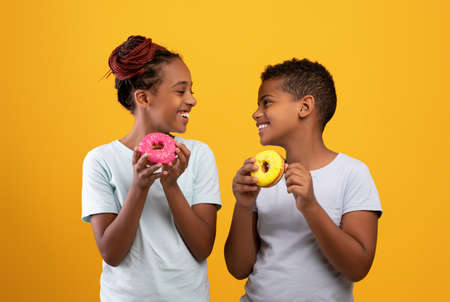 Cheerful black boy and girl eating delicious donuts