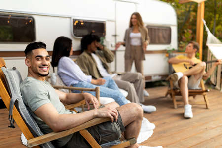 Group of multiracial young friends having outdoor party near camper van, playing guitar, having fun on autumn vacationの写真素材
