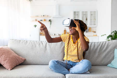 Millennial black woman using VR glasses at home