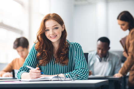 Smiling student sitting at desk in classroom posing at cameraの写真素材