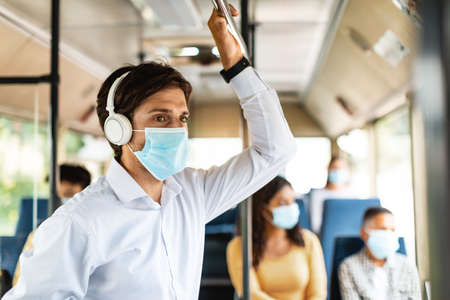 Young man in mask listening to music going by autobusの写真素材