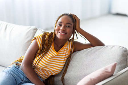 Closeup of cheerful black woman posing on couch at homeの写真素材