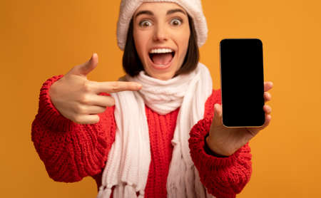I recommend. Excited lady holding and pointing at blank smartphone screen on orange studio...