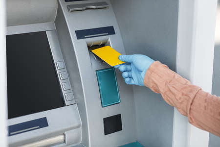 Cropped young islamic female in rubber glove inserts credit card into ATM to withdraw money outdoor, close upの写真素材