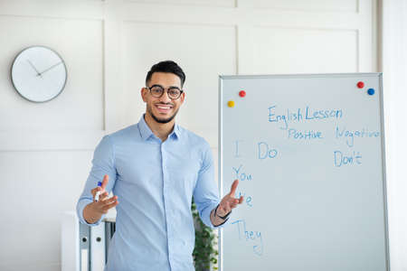 Arab male teacher giving remote class, standing near blackboard, explaining English rules to pupils from home officeの写真素材